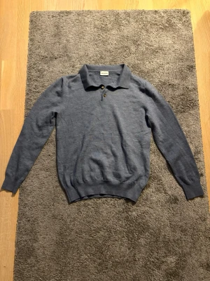 Blå tröja i ull från John Henric - Snygg blå pikétröja från John Henric i mjuk ull. Tröjan har klassisk krage och tre knappar framtill. I princip oanvänd, 