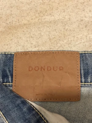 Ljusblå jeans från Dondup george - Säljer ett par ljusblå jeans från Dondup med snygga slitningar och distressed detaljer på benen. Modellen har klassisk femficksdesign, raka ben och normal passform. Jeansen är tillverkade i mjukt denim och har en skön känsla.
