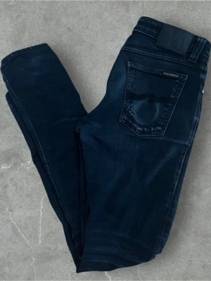 Nudie Jeans  - Storlek: 29/32 Färg: Svart Skick: Bra skick, sparsamt använda. Har en snygg, naturlig slitning vid knät för en cool, avslappnad stil. Klassiska Nudie-detaljer och ton-i-ton sömmar. Perfekta för vardag eller streetstyle!