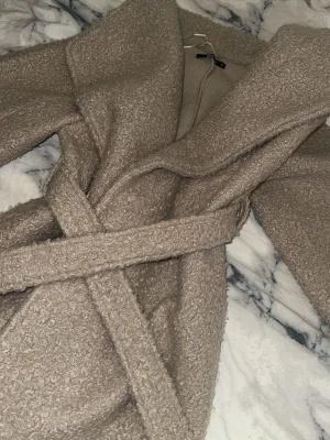 Beige teddyjacka från Gina Tricot XS - Supermjuk och mysig beige teddyjacka från Gina Tricot i storlek XS. Jackan har en oversized känsla, bred krage och knyts med bälte i midjan. Perfekt för att hålla sig varm och snygg under kyliga dagar.