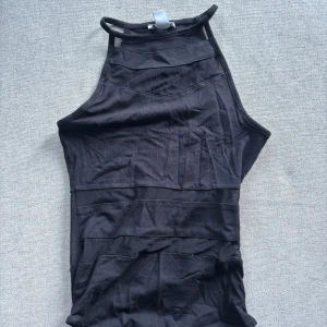 Svart ärmlös body  - Svart, tight och ärmlös body med hög hals och meshdetaljer upptill. Snyggt figurnära passform och stilren design som ger en modern vibe. Perfekt för dig som gillar minimalistiska plagg med edge.