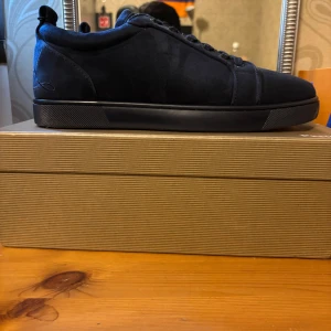 Mörkblå sneakers från Christian Louboutin - Snygga mörkblå sneakers från Christian Louboutin i mocka med klassisk rund tå och platt sula. Skorna har ton-i-ton snörning och diskreta sömdetaljer. Perfekta för dig som vill ha en stilren och lyxig look med exklusiv känsla.