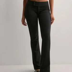 Svarta bootcut byxor från Nelly - Svarta bootcut byxor från Nelly med två knappar i midjan och klassisk passform. Byxorna har låg midja och är tillverkade i ett mjukt, stretchigt material byxor. Helt oanvända😍 nypris 350kr