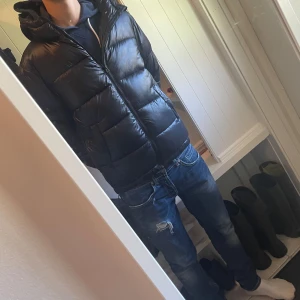 Svart pufferjacka - Säljer en helt ny svart pufferjacka från Grunt med glansig finish och huva. Jackan har dragkedja framtill, två snedställda fickor och elastiska muddar vid ärmsluten. Perfekt för kalla dagar och riktigt snygg. Köpt för 1200.      Storleken är L men passar dig som är M.    