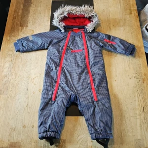 Blå vinteroverall från Kappahl - Blå vinteroverall med rött innerfoder och fuskpäls på luvan i storlek 74. Finns mindre tecken på användning vid krage och muddar. Använd i vagn så inga andra märken/slitage Finns vad jag kan se.
