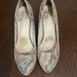 Beige pumps med ormskinnsmönster - Snygga pumps från Franco i beige med ormskinnsmönster. Skorna har spetsig tå och medelhög klack, vilket ger en elegant look. Tillverkade i syntetmaterial med struktur som påminner om reptilskinn. Perfekta för dig som vill sticka ut med en trendig detalj.