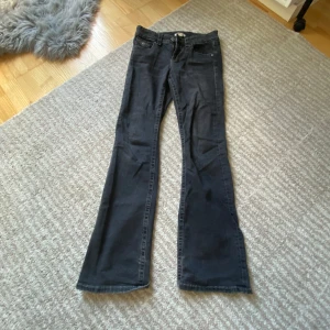 Svarta bootcut jeans från Gina Tricot - Svarta jeans från Gina Tricot med bootcut-modell och klassiska fem fickor. Jeansen har låg midja och är tillverkade i ett mjukt bomullstyg med lite stretch. Snygga detaljer med knappar och fickor bak.