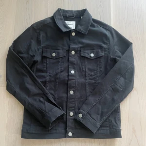 Svart jeansjacka från Jack & Jones - Svart jeansjacka från Jack & Jones med klassisk krage, silverfärgade knappar och två bröstfickor. Jackan har en rak passform och är tillverkad i bomull. Perfekt för dig som gillar en stilren look! Storlek M och passar TTS, modellen är 175cm och väger 72kg! Vid fler frågor eller funderingar tveka inte på att skriva! 