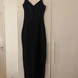 Svart långklänning med slits - Snygg svart långklänning med smala axelband och v-ringning framtill. Klänningen har en rynkad detalj vid bysten och en slits på sidan.