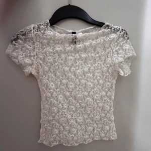 Vit spetsblus🤩 - Säljer en söt vit blus i spets med blommigt mönster. Blusen är genomskinlig, har korta ärmar och en tight passform. Perfekt att styla lager på lager eller med ett linne under💕PS: köp gärna med Instabox, postar snabbare då (Inom 24h)🥰