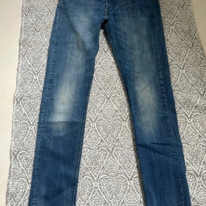 Blå jeans från Lee med raka ben - Säljer ett par klassiska blå jeans från Lee med raka ben och normal passform. Jeansen har snygga slitningar framtill, fem fickor och Lee-logga på bakfickan samt läderpatch i midjan. Perfekta för dig som gillar en tidlös denimlook.