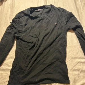 Svart långärmad tröja Tommy Hilfiger - Svart långärmad tröja från Tommy Hilfiger i ekologisk bomull. Klassisk design med liten logga på bröstet och rund halsringning. Perfekt för dig som gillar stilrena och enkla plagg med en touch av premiumkänsla.