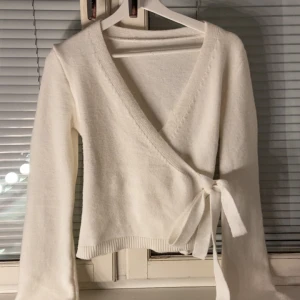 Vit omlottkofta med knytband - ‼️‼️PRIS KAN SÄNKAS‼️‼️Superfin vit omlottkofta med knytband i midjan och v-ringad hals. Koftan är stickad och har långa ärmar samt ribbade muddar. Perfekt för lager på lager och ger en clean och fräsch look.