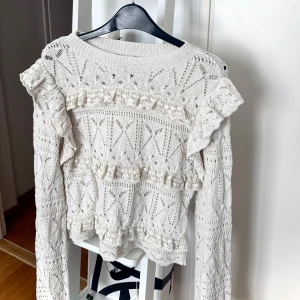 Vit stickad volangtröja från Zara - Supersöt vit/beige stickad tröja från Zara med volangdetaljer och spets längs tröjan. Tröjan har ett väldigt fint mönster, rund halsringning och långa ärmar som är lite utsvängda där nere . Tröjan är använd men det finns inga defekter på den💗
