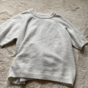 Vit stickad kortärmad tröja - Supermjuk vit stickad tröja med korta ärmar och rund hals. Perfekt för lager-på-lager och chill vår- eller sommarstil. Ribbstickade muddar vid ärmslut och nederkant ger en clean look.