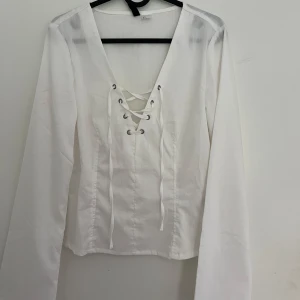 Vit långärmad blus med snörning - Säljer SNYGGASTE vita långärmade blusen med djup v-ringning och snygg snörningsdetalj framtill. Toppen har en figurnära passform och trumpetärmar. Ger en lite korsettliknande look verkligen skitsnygg. Aldrig använd utan endast testad och slutsåld!!!