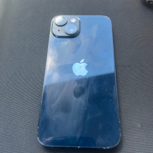 iPhone 14 - Snygg iPhone 13 i blått, fullt fungerande med dubbla kameror och Face ID. Skärmen och baksidan har några synliga fingeravtryck och lättare ytslitage, men inga större repor eller sprickor. Perfekt för dig som vill ha en kraftfull och modern smartphone.