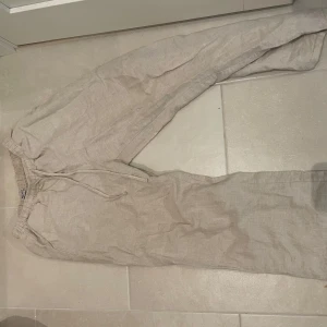 Beiga linnebyxor från Madlady - Säljer ett par beiga linnebyxor från Madlady i storlek small. Byxorna har resår i midjan och snörning för extra komfort. Perfekta för chill dagar och har en avslappnad passform med raka ben. Dem är i storleken tall men de har blivit kortare i tvätten