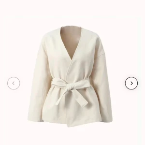 Beige omlottjacka med bälte - Stilren beige omlottjacka med knytbälte i midjan och v-ringad hals. Jackan har lång ärm och en avslappnad passform, perfekt för lager-på lager. Enkel och clean design som passar till många outfits.