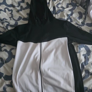 Nike svartvit hoodie med dragkedja - Nike hoodie i svart och vitt med hel dragkedja framtill. Tröjan har huva med snörning och Nike-logga på bröstet. Perfekt för dig som gillar sportig och stilren look. Materialet känns mjukt och följsamt, passar till chill eller träning. Storlek Xl men L  passar åkså 