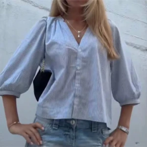 Blårandig skjorta med puffärm - Snygg blårandig skjorta med v-ringning och puffiga trekvartsärmar. Skjortan har knappar framtill och är tillverkad i ett lätt bomullstyg. Perfekt till jeans eller kjol för en fräsch look. Slut i alla storlekar! 