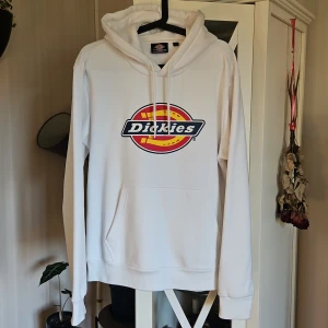 Vit hoodie från Dickies i storlek L - Säljer en clean vit hoodie från Dickies i storlek L. Klassisk modell med stor logga framtill, huva med snörning och känguruficka. Perfekt för dig som gillar streetwear och vill ha en enkel men snygg look.