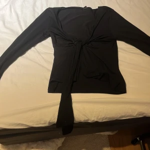 Svart omlottopp från Gina Tricot - Svart tröja från Gina som man knyter. Mycket bra skick. Säljer då den blivit för liten. Sälj inte längre vad jag kan se men köpte den för runt 400kr