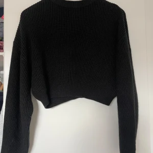 Svart croppad stickad tröja Divided - Svart croppad stickad tröja från Divided. Tröjan har en ribbad struktur, lång ärm och rund halsringning. Perfekt för lager-på-lager och passar till både jeans och kjol.