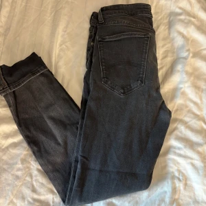Svarta skinny jeans från Tommy Hilfiger - Säljer ett par svarta skinny jeans från Tommy Hilfiger med klassisk femficksdesign och snygga detaljer som röd knapp och diskret logga. Jeansen har en smal passform och är tillverkade i stretchig bomullsdenim för extra komfort.