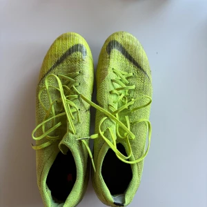Nike gula fotbollsskor med dobbar - Säljer ett par grymma fotbollsskor från Nike i neon-gult med svarta detaljer och snörning. Skorna har stickad ovandel och metall-dobbar för bästa grepp på planen. Perfekta för dig som vill sticka ut på matchen! Storlek 44,5 med skruvdobn. ACC
