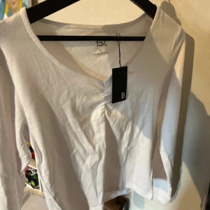Vit långärmad topp från 157 - Vit långärmad topp från 157 med v-ringning och lätt rynkdetalj framtill. Tillverkad i mjuk bomull, perfekt för en clean och enkel look. Snygg att styla med jeans eller kjol.