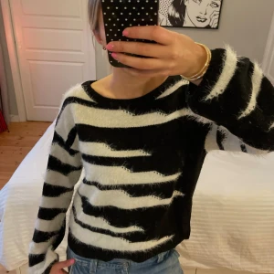 Zebramönstrad stickad tröja JDY - Säljer en fluffig stickad tröja från Jacqueline de Yong i storlek L. Tröjan har svartvitt zebramönster, rund halsringning och långa ärmar. Den är supermjuk och har en lite loose passform, perfekt för att mysa i under kyliga dagar.
