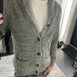 Grå stickad kofta från H&M - Säljer en grå stickad kofta från H&M i storlek M, modellen är ca 180 cm lång. Hör av dig vid funderingar!