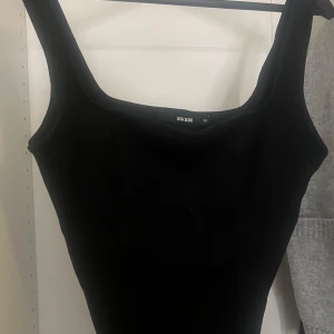 Svart cut out topp från BikBok - Säljer en svart topp från BikBok i storlek M. Toppen har breda axelband, fyrkantig ringning och en snygg cut out-detalj i midjan. 