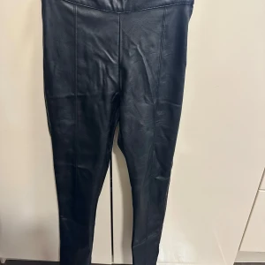 Svarta skinnbyxor från Gina Tricot - Snygga svarta skinnbyxor från Gina Tricot i storlek S. Byxorna har hög midja, smal passform och dragkedja i sidan. Perfekta för dig som vill ha en edgy look med stilren känsla. Materialet är mjukt och följsamt för en bekväm känsla hela dagen.