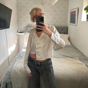 Vit croppad skjorta med knappar - Säljer en vit croppad skjorta med v-ringning och knappar framtill. Skjortan har långa ärmar och en avslappnad passform. Från misslisibelles kollektion med nakd