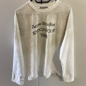 Vit långärmad tröja Acne Studios - Säljer en vit långärmad tröja från Acne Studios med svart tryck på bröstet där det står 'Acne Studios Stockholm 1996'. Tröjan har en avslappnad passform och är tillverkad i mjuk bomull. Perfekt för en clean och stilren look. Tröjan är använd 1 gång och säljs för att den inte passa mig
