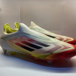 Adidas f50 Elite laceless SG ”Pure victory”  - Säljer ett par Adidas X Speedflow fotbollsskor i en snygg mix av vitt, rött och neon-gult. Skorna har en strömlinjeformad design utan snörning, med platt sula och rund tå. Ovandelen är tillverkad i syntetmaterial för lätt vikt och bra grepp på planen. SKRIV FÖR FLER BILDER 