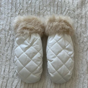 Vita vantar med päls - Säljer ett par vita vantar med mjuk beige fuskpäls vid mudden. Vantarna har ett snyggt rutmönster på ovansidan och är perfekta för kalla vinterdagar. De har en klassisk tumdesign och elastisk kant för bra passform.