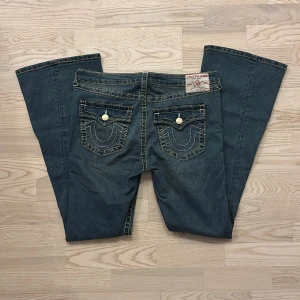 True Religion jeans Joey💙 - Snygga blå jeans från True Religion, modell Joey Mid Rise Flare. Jeansen har markerade kontrastsömmar, utsvängda ben och ikoniska fickor med lock och guldiga knappar. Klassisk femficksdesign i robust bomullsdenim.
