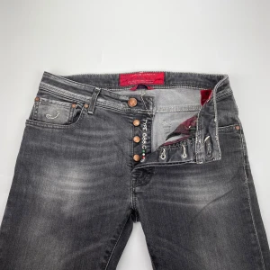 Jacob Cohen jeans 688 - Snygga grå jeans från Jacob Cohen med slitna detaljer och kontrastsömmar. Klassisk femficksmodell med knappar i gylfen och svart patch med broderad logga bak. Jeansen har en cool tvättad look och är tillverkade i mjukt denimtyg.