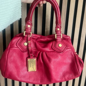 Marc Jacobs väska - röd  - Marc Jacobs classic q baby groove med guldiga detaljer. Väskan är röd. Axelremband ingår ej. Dustbag ingår. Den är ca 30 cm bred och är i den lilla modellen. Mycket bra skick. Finns en liten fläck på lädret, se bilder. Fler bilder finns och svarar gärna på frågor ❤️