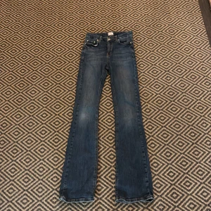 Blå bootcut jeans från GRUNT - Snygga blå jeans från GRUNT med klassisk bootcut-modell. Jeansen har fyra fickor, bälteshällor och dragkedja med knapp. Materialet är slitstarkt denim i bomull och passformen är normal med lätt utsvängda ben.