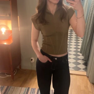 Beige topp från Zara - Cool och unik mörkbeige topp från Zara med korta ärmar och hög krage. Toppen är ribbad och har en dragkedja framtill. Snygg figurnära passform och tillverkad i stretchigt material.