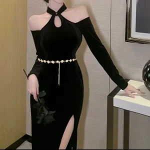 Svart sammetsklänning med slits - Elegant svart långklänning i sammet med offshoulder och lång ärm. Klänningen har en snygg slits framtill, pärlformad bälte i midjan och en unik halterneck med cut-out vid halsen. Figurnära passform som framhäver siluetten och ger en lyxig känsla.