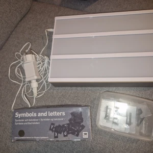 Lightbox med bokstäver och symboler - Ljusskylt med tre rader, komplett med bokstäver, siffror och symboler. Fungerar utmärkt, med strömbrytare och nätadapter. Perfekt för personliga meddelanden och dekoration. Aldrig kommit till användning mer än att fota för att visa att den funkar. Förpackningen på de mörka bokstäverna har blivit sliten pga legat I en låda med annat. Går att användas utan sladd med batterier oxå. 