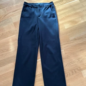 Svarta kostymbyxor med raka ben - Snygga svarta kostymbyxor med raka ben och klassisk passform. Byxorna har hällor för bälte, snedställda fickor fram och är tillverkade i ett mjukt tyg som ger en dressad look. Perfekta för dig som gillar stilrena och tidlösa plagg.