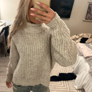 Beige stickad polotröja - Supermysig beige stickad polotröja med grov ribbad struktur och lång ärm. Tröjan har en hög krage och en loose fit som ger en chill och avslappnad vibe. Perfekt att slänga på sig när det är kallt ute.