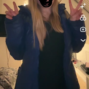 Blå pufferjacka med huva från QS - Snygg blå pufferjacka från QS med huva och dragkedja framtill. Jackan har quiltade detaljer och en cool glansig finish. Perfekt för kalla dagar när du vill hålla stilen. Fodrad insida och praktiska fickor.