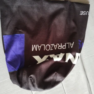 Svart mössa med Xanax-tryck - Svart mössa med stort vitt och lila tryck som liknar en Xanax-förpackning. Texten är tydlig och designen sticker ut med medicinskt tema. Materialet känns som mjuk polyester, perfekt för dig som gillar unika och edgy accessoarer.